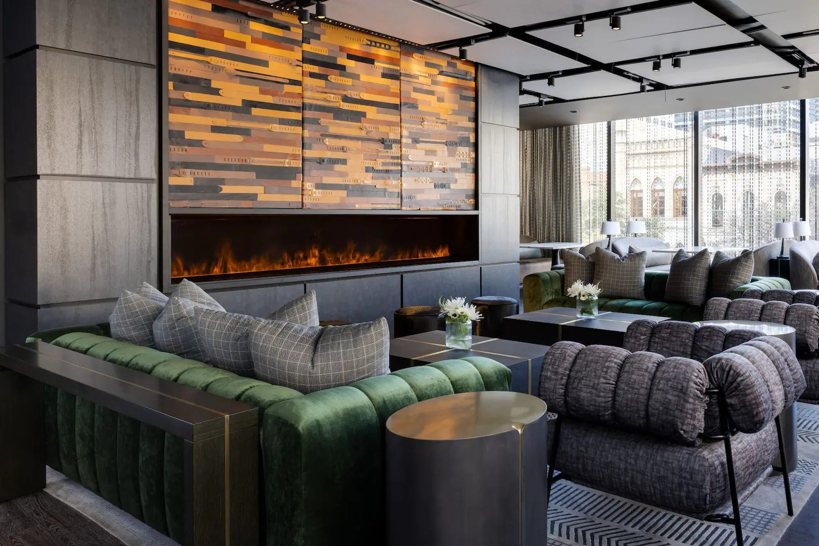 Modern lounge area with green and gray sofas, a fireplace, and large windows.