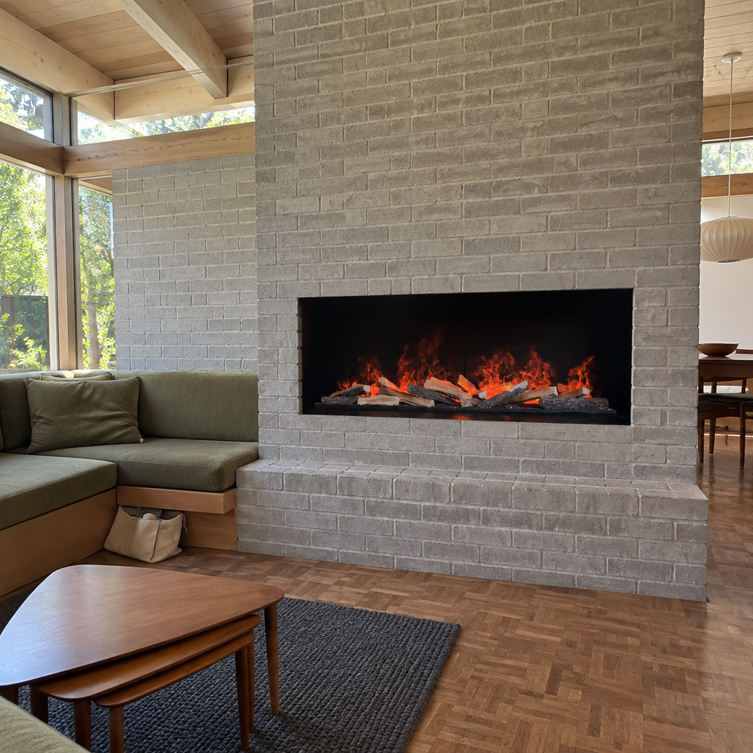 A modern linear fireplace with glowing orange flames set into a light gray stone brick wall, shown in a contemporary living room with a green sectional sofa and wood flooring.