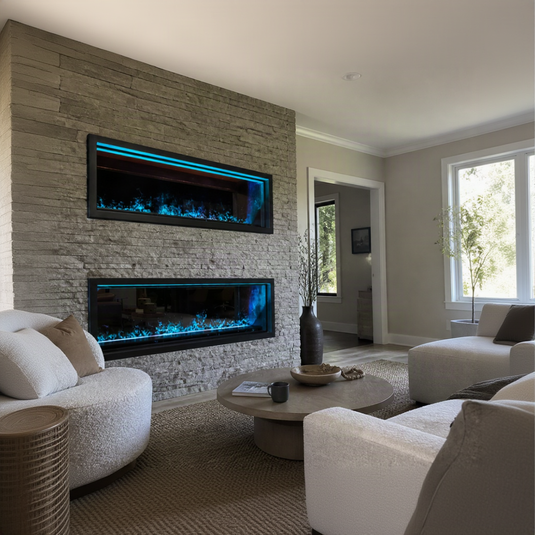 A modern living room featuring two long rectangular electric Aquafire Pro Water Vapor Fireplace mounted on a textured stone wall, with bright blue flame effects. The room includes light-colored upholstered seating, a round coffee table, and large windows.
